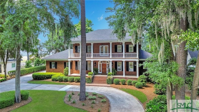 view of front of property featuring brick siding, a front yard, a balcony, curved driveway, and covered porch