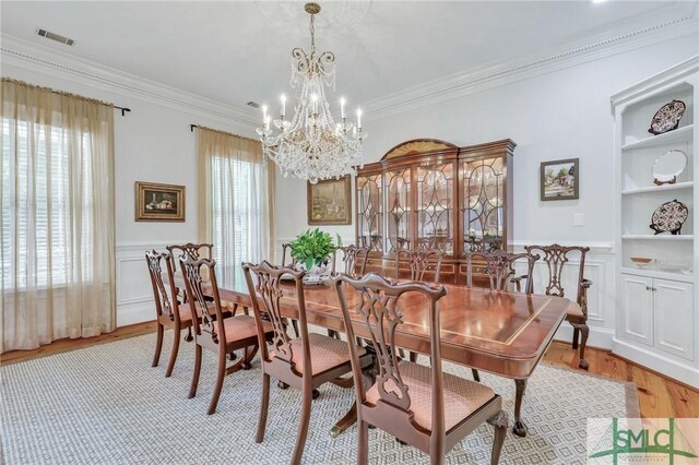 dining area with a decorative wall, a notable chandelier, ornamental molding, and light wood-style floors