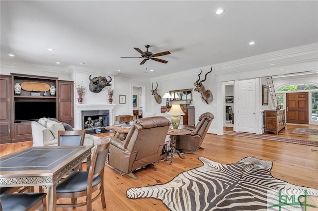 living room featuring ceiling fan, a fireplace, light wood-style floors, ornamental molding, and recessed lighting