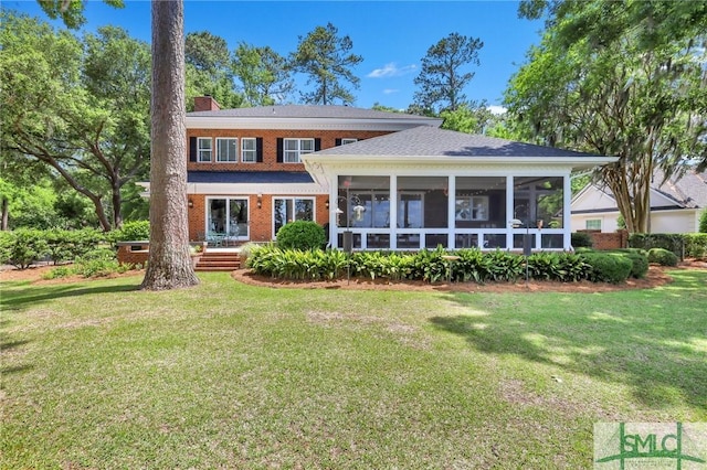 rear view of property featuring a yard, a chimney, a sunroom, and brick siding