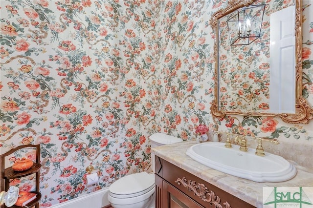 half bathroom with vanity, toilet, and wallpapered walls