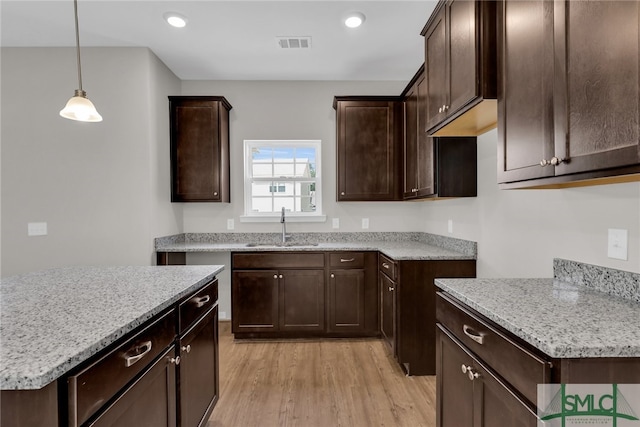 kitchen with visible vents, dark brown cabinetry, light stone counters, a sink, and light wood finished floors