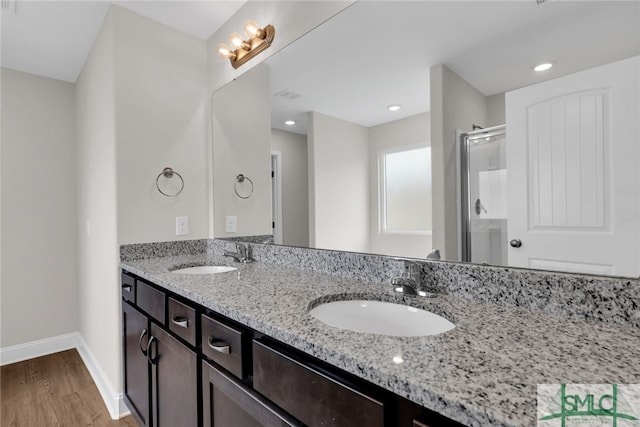 full bathroom with double vanity, a stall shower, a sink, and wood finished floors