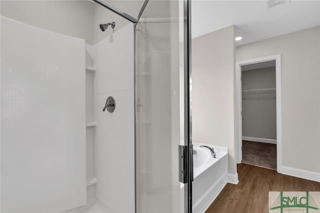 full bathroom with a bath, visible vents, a stall shower, wood finished floors, and baseboards