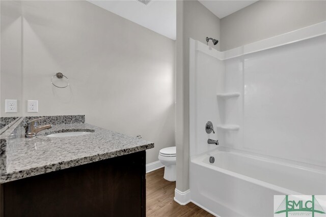 bathroom featuring wood finished floors, vanity, baseboards, toilet, and tub / shower combination