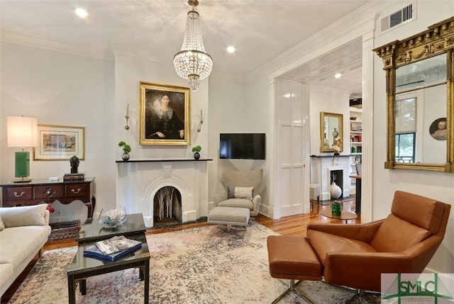 living room featuring visible vents, crown molding, wood finished floors, a fireplace with raised hearth, and a chandelier