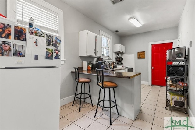 724 E 49th St, Savannah, GA 31405 - kitchen featuring a peninsula, light tile patterned flooring, dark countertops, white appliances, and white cabinetry