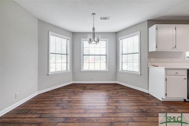 unfurnished dining area featuring an inviting chandelier, dark wood-style floors, a textured ceiling, and visible vents