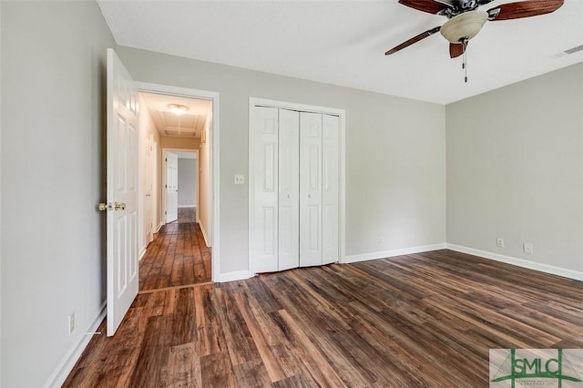 unfurnished bedroom featuring a closet, baseboards, attic access, and dark wood-style floors