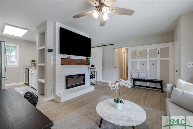 living area featuring baseboards, a ceiling fan, light wood finished floors, and a barn door