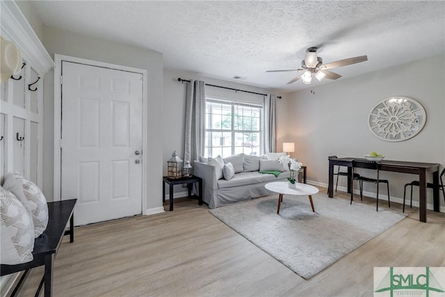 living room with baseboards, a ceiling fan, light wood-style flooring, and a textured ceiling