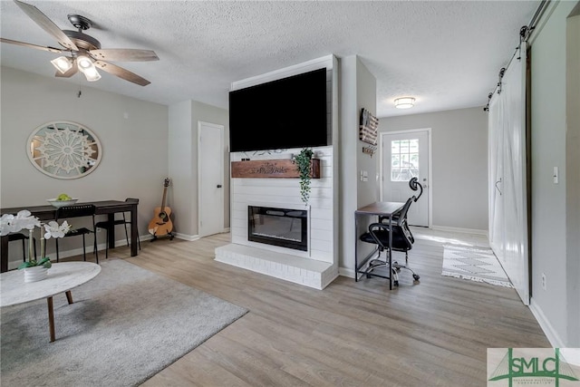 living area featuring ceiling fan, a barn door, a textured ceiling, a large fireplace, and wood finished floors