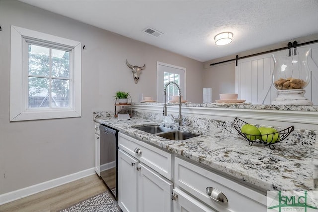 kitchen with a barn door, a sink, dishwasher, light wood-style flooring, and visible vents