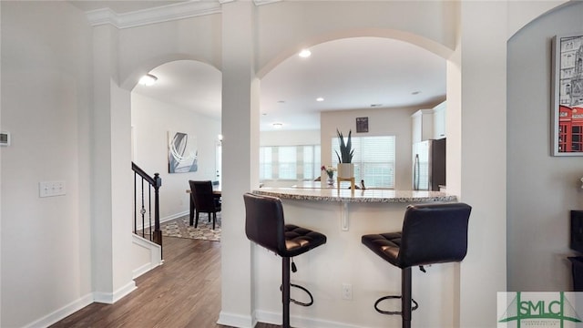 kitchen with a kitchen bar, arched walkways, white cabinets, freestanding refrigerator, and dark wood-style floors