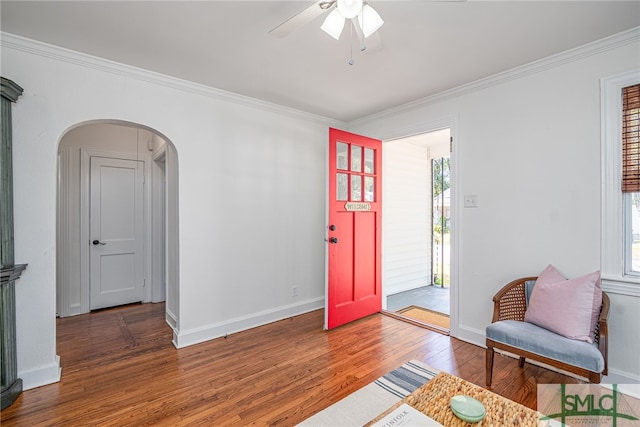 entrance foyer with crown molding, arched walkways, a ceiling fan, and wood finished floors