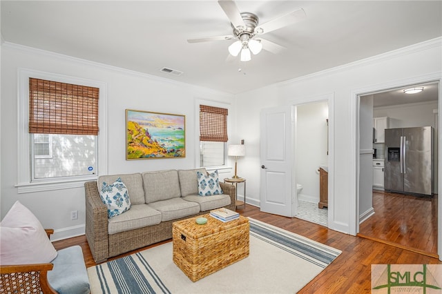 living room with visible vents, ornamental molding, wood finished floors, baseboards, and ceiling fan