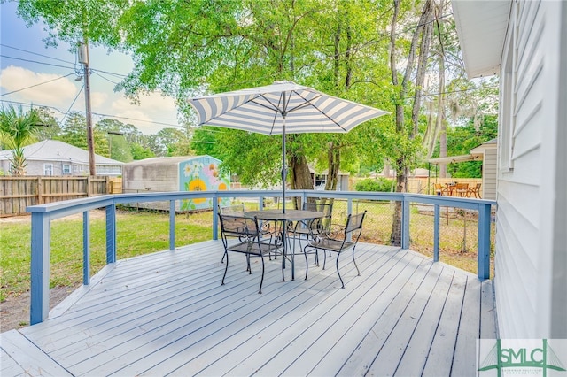 deck featuring outdoor dining area, a fenced backyard, a yard, a storage shed, and an outbuilding