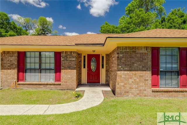 view of exterior entry with a lawn, roof with shingles, and brick siding