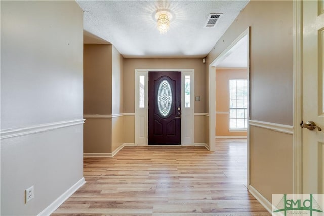 foyer entrance with visible vents, a textured ceiling, light wood finished floors, and baseboards