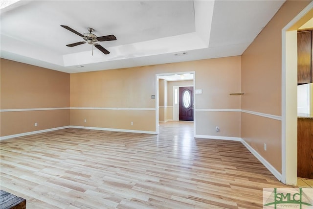 empty room with baseboards, ceiling fan, a tray ceiling, and light wood finished floors