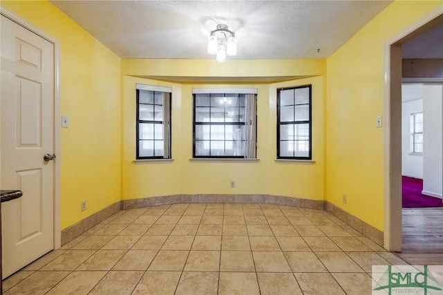 unfurnished room featuring light tile patterned floors, baseboards, and a textured ceiling