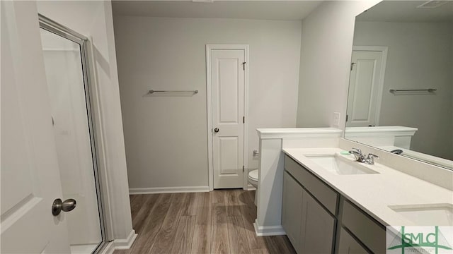 bathroom featuring double vanity, a stall shower, wood finished floors, a sink, and toilet