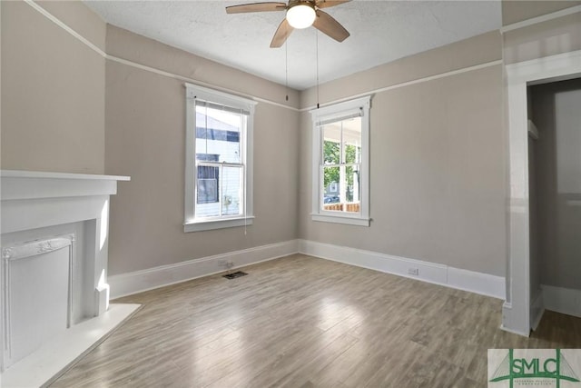 unfurnished living room with visible vents, wood finished floors, baseboards, ceiling fan, and a textured ceiling