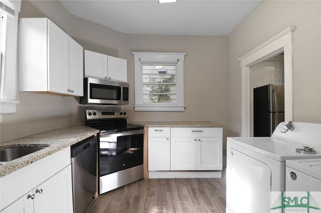 kitchen featuring washer and dryer, stainless steel appliances, white cabinetry, and light wood-type flooring