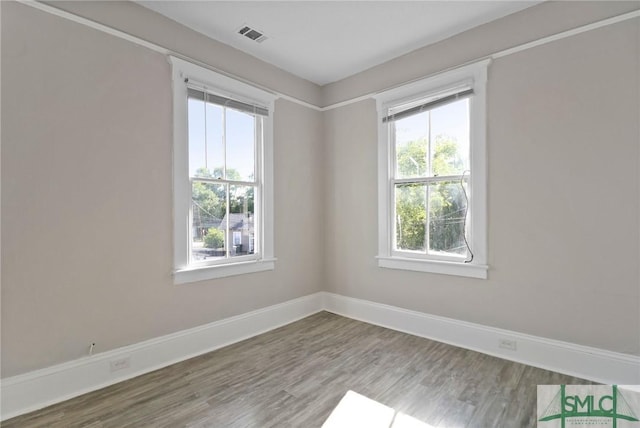 spare room featuring baseboards, visible vents, plenty of natural light, and wood finished floors