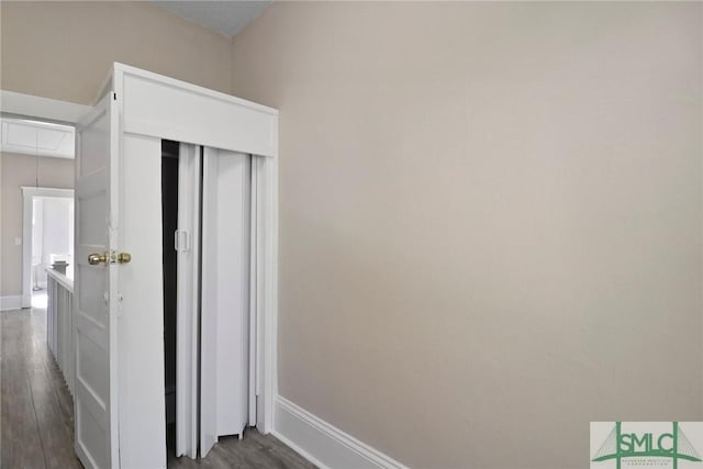 hallway with baseboards, dark wood finished floors, and attic access
