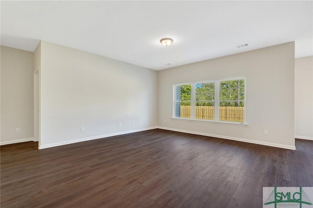 unfurnished room featuring baseboards, visible vents, and dark wood finished floors