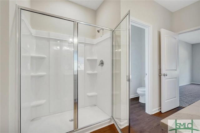 bathroom featuring toilet, baseboards, wood finished floors, and a stall shower