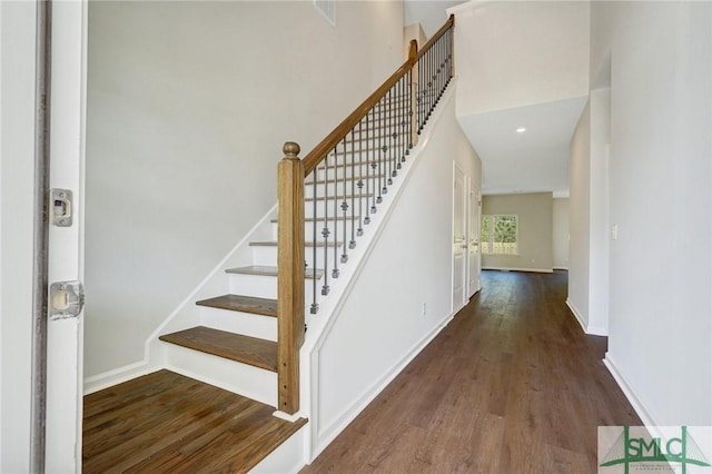 staircase featuring visible vents, a high ceiling, baseboards, and wood finished floors