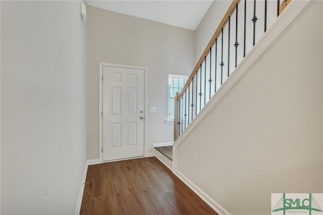 foyer entrance with baseboards, a high ceiling, stairs, and wood finished floors