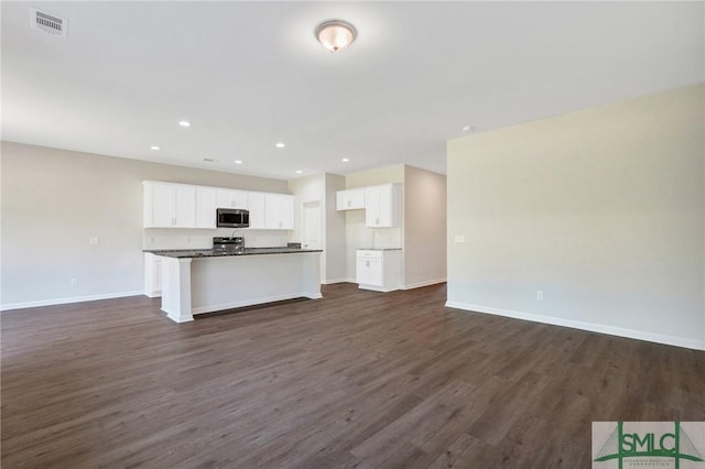 kitchen with white cabinetry, stainless steel microwave, open floor plan, and dark countertops