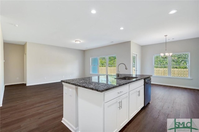 kitchen featuring a sink, a kitchen island with sink, dark wood finished floors, dark stone counters, and stainless steel dishwasher
