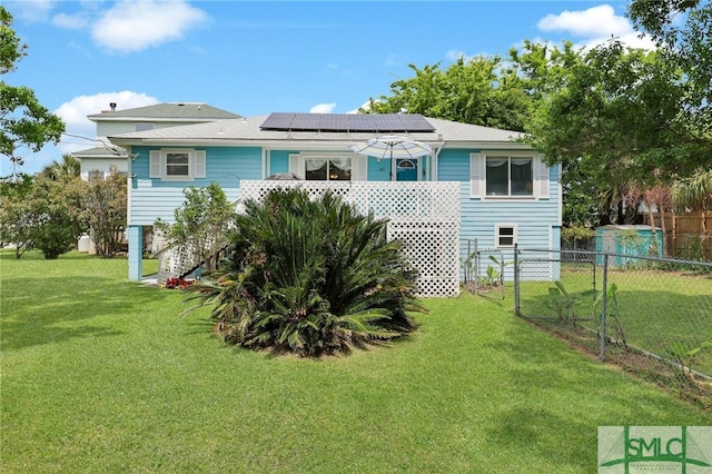 106 Pelican Ct, Tybee Island, GA 31328 - rear view of property featuring a yard, fence, a shingled roof, and roof mounted solar panels
