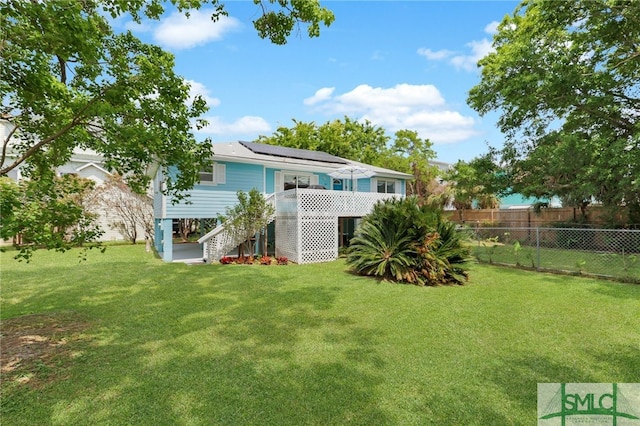 106 Pelican Ct, Tybee Island, GA 31328 - rear view of property featuring a lawn, roof mounted solar panels, fence, and stairs