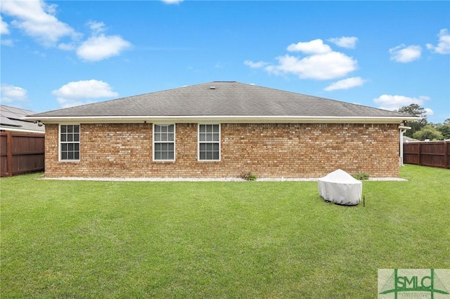 back of house featuring brick siding, a fenced backyard, roof with shingles, and a yard