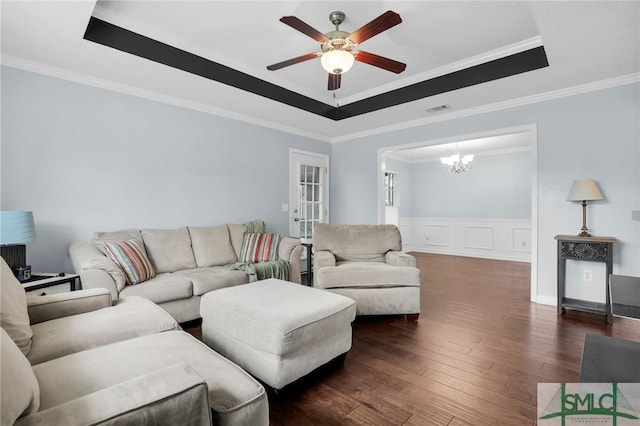 living room featuring dark wood-style flooring, visible vents, a raised ceiling, ceiling fan with notable chandelier, and ornamental molding