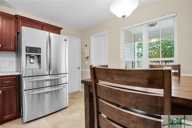 kitchen with stainless steel fridge, decorative backsplash, reddish brown cabinets, and light countertops