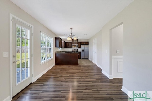 kitchen with dark brown cabinetry, dark wood finished floors, a peninsula, a notable chandelier, and stainless steel appliances