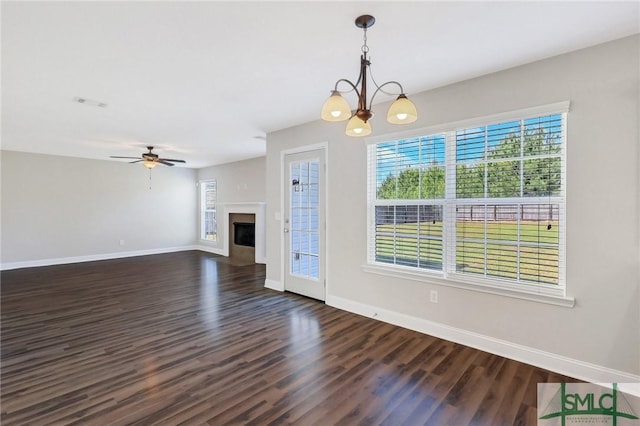 unfurnished living room featuring baseboards, dark wood-style floors, ceiling fan with notable chandelier, and a fireplace