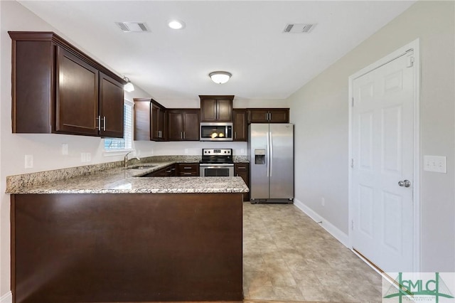kitchen featuring appliances with stainless steel finishes, light stone countertops, dark brown cabinets, a sink, and a peninsula