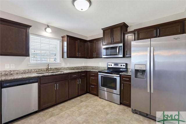 kitchen with light stone counters, a sink, appliances with stainless steel finishes, and dark brown cabinetry
