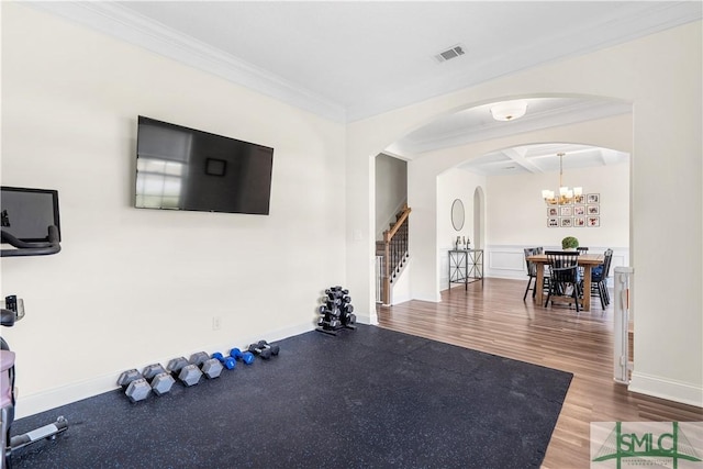 exercise area featuring arched walkways, ornamental molding, wood finished floors, and visible vents