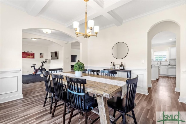 dining space with wood finished floors, ornamental molding, beam ceiling, and a notable chandelier