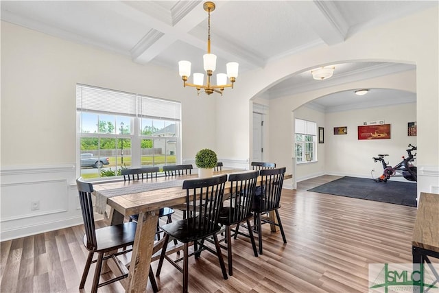 dining space featuring a notable chandelier, arched walkways, wood finished floors, beamed ceiling, and ornamental molding