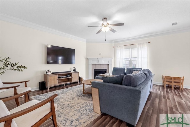 living area featuring crown molding, ceiling fan, dark wood finished floors, a tiled fireplace, and visible vents