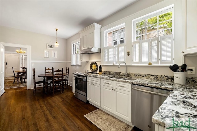 kitchen featuring dark wood-style floors, under cabinet range hood, a sink, appliances with stainless steel finishes, and a notable chandelier